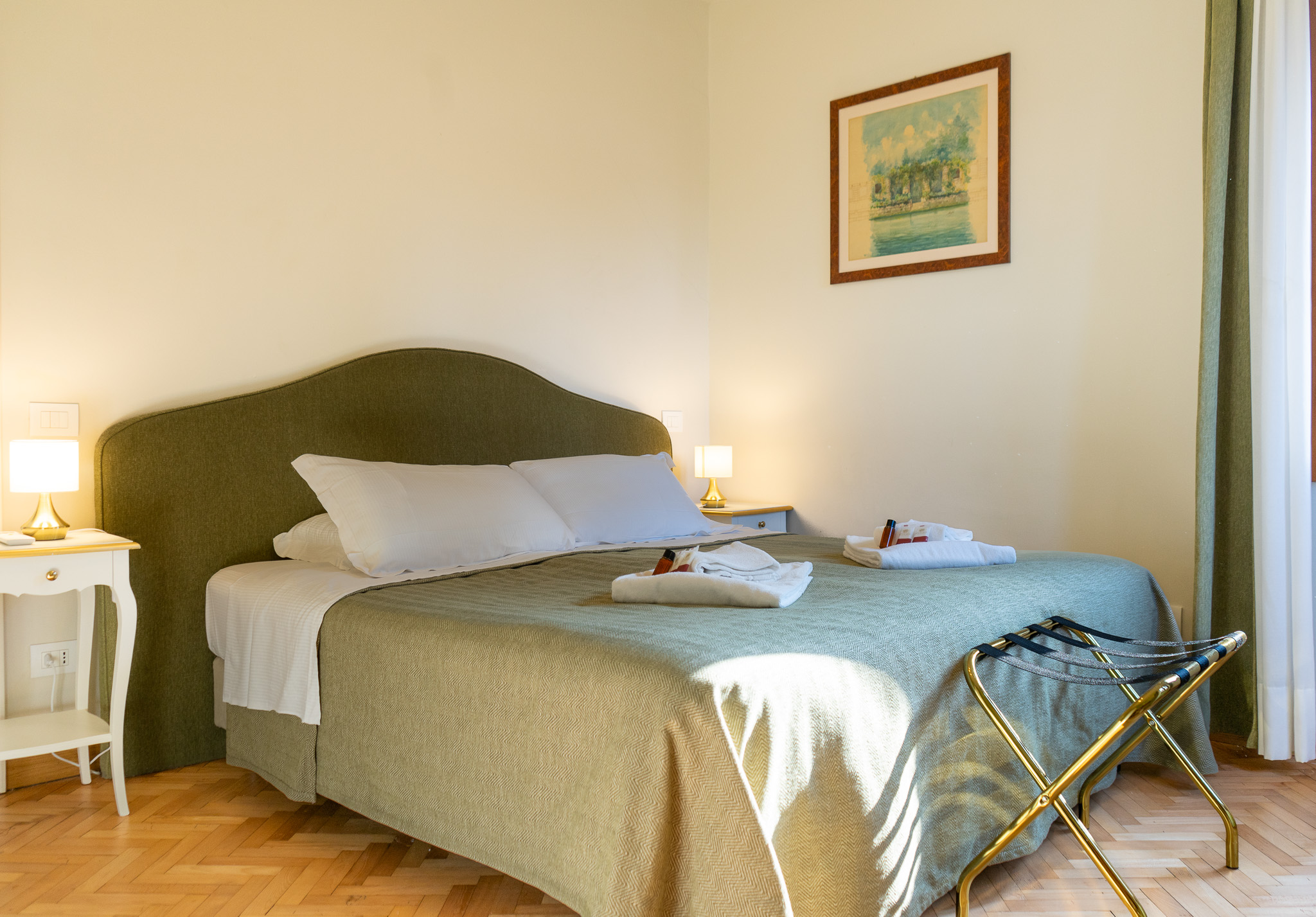 Master bedroom Emerald apartment Venice - green upholstered headboard, brass lamp, herringbone parquet